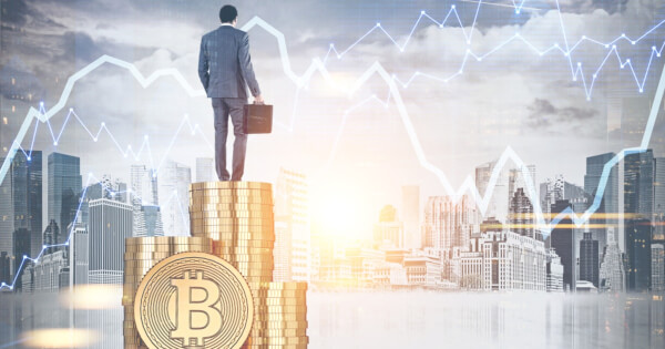 businessman atop a pile of Bitcoins overlooking a city background and stock chart